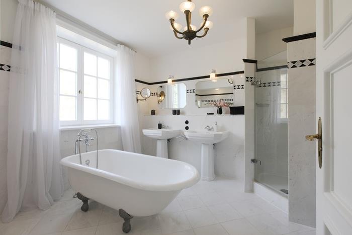 laisvai stovinti vonia seno stiliaus vonios kambarys dviguba kriauklė pjedestalo kriauklė veidrodis ilgos baltos užuolaidos baltos plytelės