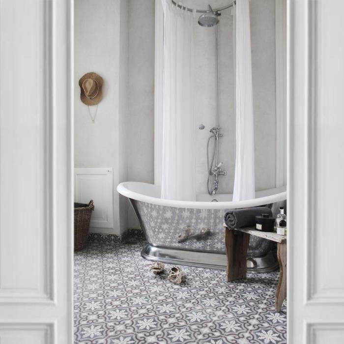 cemento plytelių grindų danga su subtiliais arabesko raštais ir chromuota vonios išvaizda sukuria prašmatnią atmosferą šiame vienspalviame vonios kambaryje