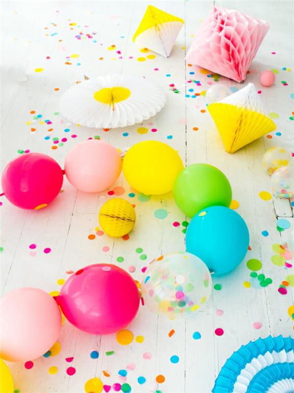 eilutė ryškiaspalvių balionų, dekoratyvinės popierinės pinatos, konfeti ant baltų lentų grindų