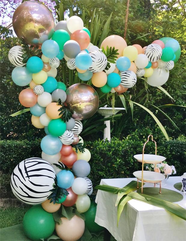 balionai sodo vakarėliui, didelė balionų arka, žalios gyvatvorės ir atogrąžų augalai, stalas