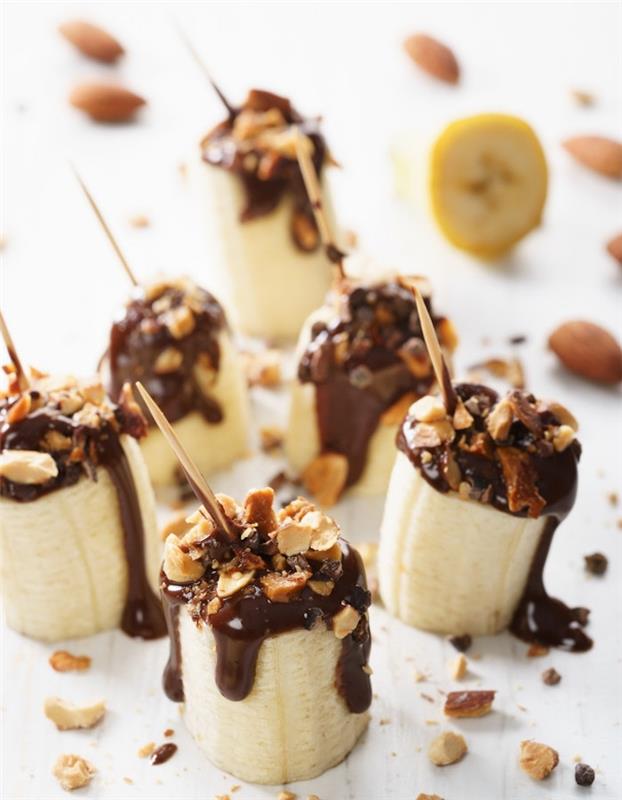 Saldi Kalėdų linksmybių idėja, pusiau šaldytas šokoladinis bananas ir žemės riešutai ant dantų krapštuko