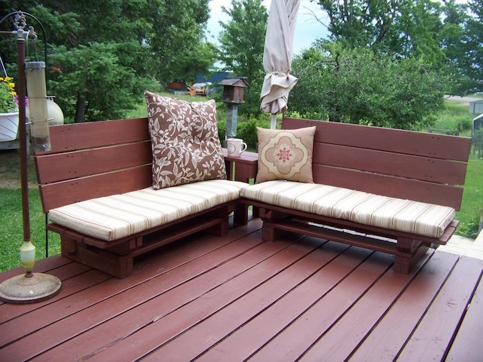 Açık ahşap terasta bej ve kahverengi koltuk minderleri ile kahverengiye boyanmış ahşap palet tezgahı