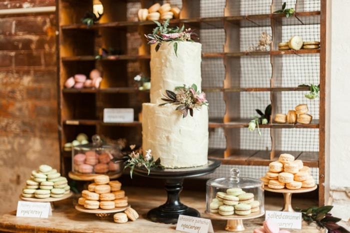 podeželska elegantna dekoracija sladkarij, dvotirna poročna torta, cvetlični okraski makroni v vrstah v izložbah za torte, ozadje omare iz lesa, kmečka miza