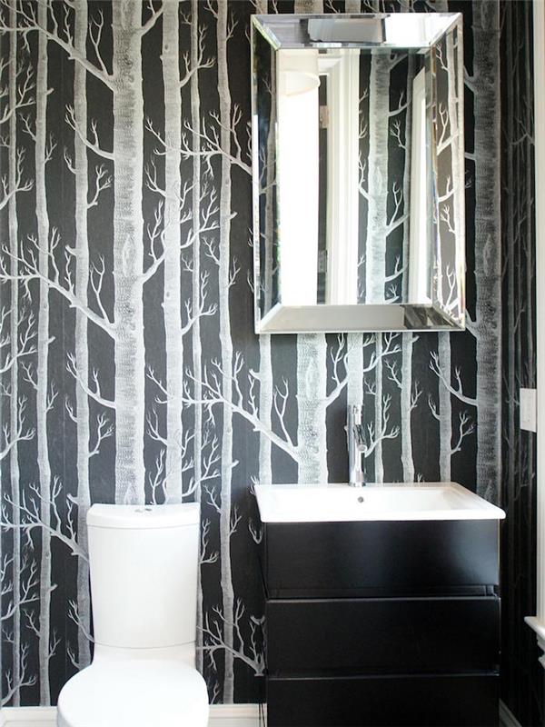 prenova kopalnice, temno ozadje, okrašeno s svetlo sivo poslikanimi drevesi brez listov, sodobno belo straniščno školjko in črno komodo z belim umivalnikom
