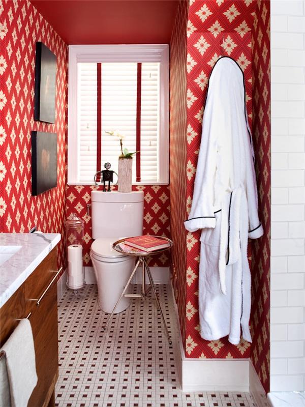 ideje za majhno kopalnico, stranišče z ozadjem z rdečimi in belimi vzorci, tla z majhnimi mozaičnimi ploščicami, lesena omara z belim umivalnikom, belo stranišče in okno z žaluzijami