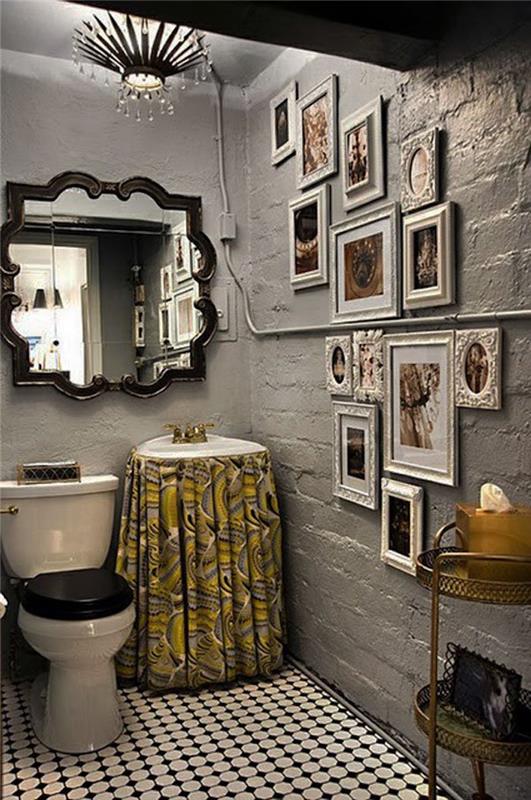 stranišče s hrapavimi stenami, pobarvanimi v sivi barvi, z velikim baročnim stenskim ogledalom, eno steno, okrašeno s številnimi fotografijami v različnih belih okvirjih, belimi in črnimi keramičnimi tlemi, klasičnim WC sedežem in umivalnikom z rumeno -sivo zaveso z vzorcem