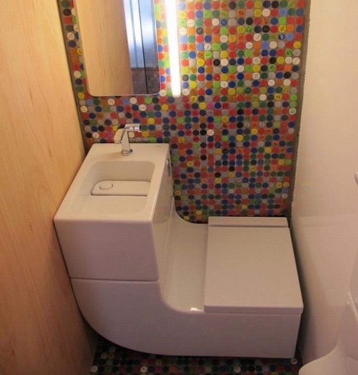 prenova kopalnice, majhen prostor z belim umivalnikom in WC sedežem v enem, ena stena je pokrita z bledo leseno desko, ena je bela, druga pa okrašena z večbarvnim mozaikom z ogledalom in svetlobo