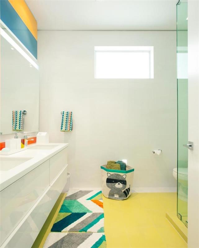 prenova kopalnice, prostorna kopalnica z velikim, belim dvojnim umivalnikom, pastelno rumena tla, štirimi barvnimi preprogami, velikim ogledalom in modro -rumenimi črtami na steni nad