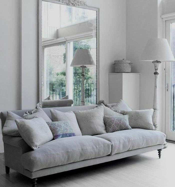 didelis veidrodis, pilka sofa -lova, pilkos pagalvės, baltos sienos, medinės grindys