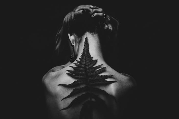 Ženska z drevesnimi listi na hrbtu, ideja o temnem ozadju, elegantna enobarvna fotografija za uporabo na mobilnem telefonu