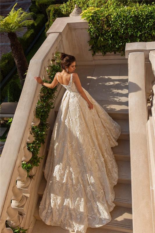 Poročna obleka princese brez naramnic z dolgim ​​vlakom, lepa ženska v beli čipkasti obleki na fotografiji na stopnicah stanovanja
