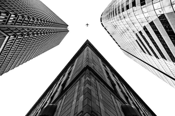 čudovita črno -bela fotografija letala na nebu med tremi visokimi stavbami, mestna pokrajina z izvirno perspektivo