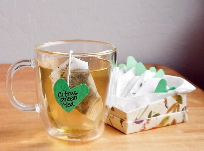kaj podariti najboljši prijateljici za rojstni dan, skodelica iz prozornega stekla, ki vsebuje čaj in vrečko, z ročno izdelano zeleno etiketo v obliki srca, več vrečk čaja v bližnji škatli
