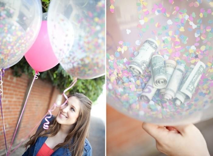 kul darila za najstnike, nasmejana rjavolaska, ki drži roza balon in dva prozorna balona, ​​napolnjena s konfeti, od blizu eden od prozornih balonov razkriva več zvitih dolarjev