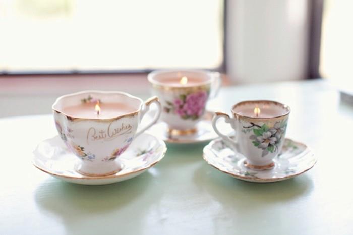 božična darila najboljši prijatelj, tri poslikane porcelanske skodelice in krožniki z prižganimi rožnatimi svečami na bledo modri površini