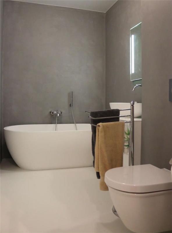 Gri mumlu beton duvar, beyaz karo zemin ve oval bağımsız küvet ile modern tarzda yenilenmiş banyo