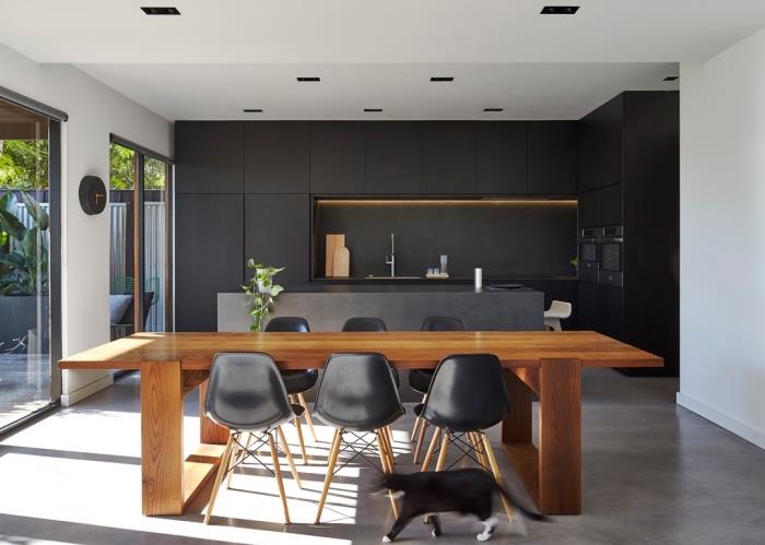 virtuvės modelis su centrine betono dizaino sala, atvira į valgomąjį su stačiakampiu rudu mediniu stalu