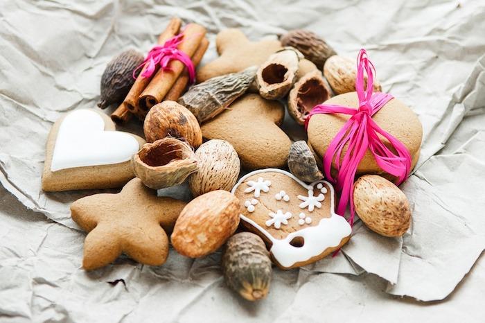 sausainiai, sausainiai, riešutai ir cinamonas su rausva virvelės puošmena ant paprasto popieriaus lapo, gurmaniški kalėdiniai tapetai