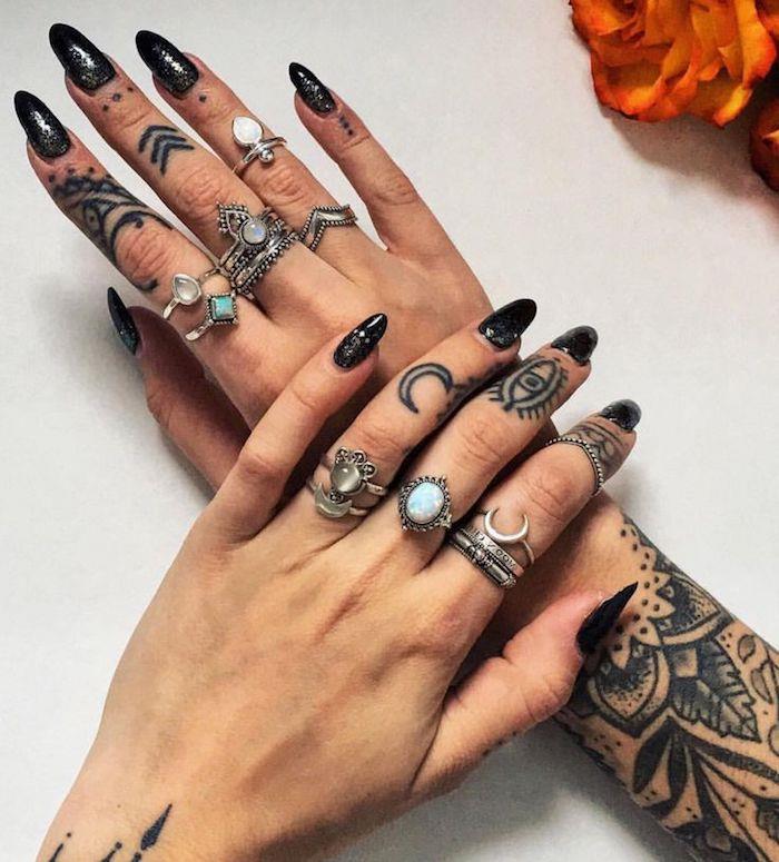 dolgi črni nohti, veliko srebrnih prstanov, tetovaže mandale na obeh rokah, tetovaže z prstani