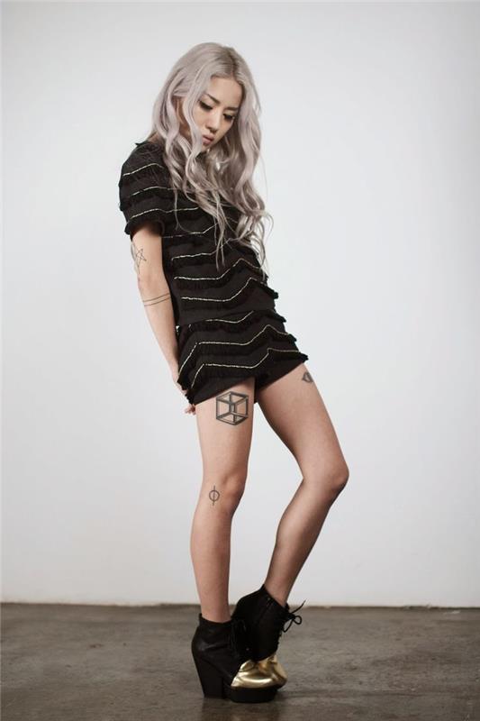 črna obleka in čevlji, dolgi platinasto blond lasje, tetovaža cvetja življenja, 3d tetovaža s kvadratnim stegnom