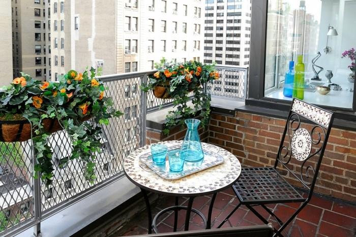 üst kısmı mozaik efektli yuvarlak metal masa, mavi bardak ve sürahi içeren tepsi, uygun sandalyenin yanında, turuncu saksı çiçekleri