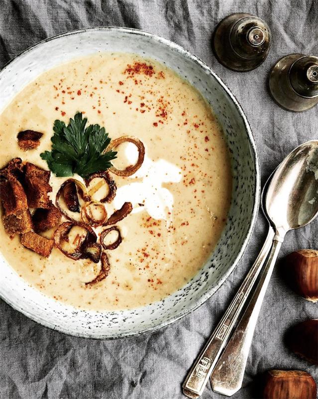 gri masa örtüsü, çorba dolu seramik kase, tavuk tortellini çorbası, tuz ve karabiber, yanında iki kaşık