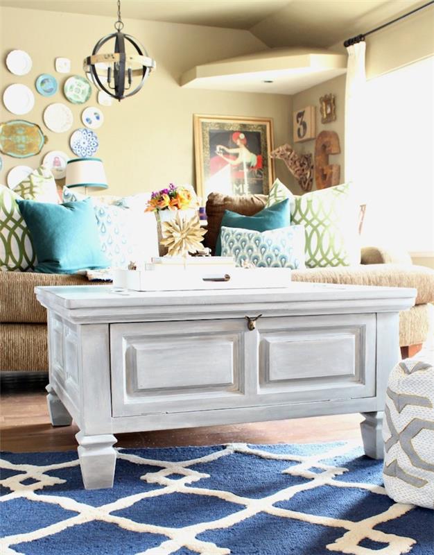 Baltas kavos staliukas, mėlynos ir baltos spalvos geometrinis kilimas, smėlio spalvos virtuvės spintelės tapyba, perdažyta spalvota medinė spintelė