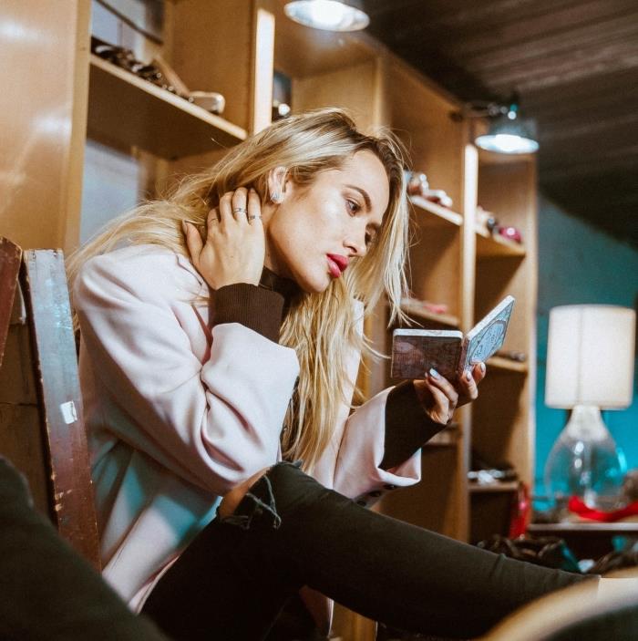 blondinka na rjavolaski z dolgimi tankimi lasmi, obleka v pastelno roza plašču z rjavim puloverjem in črnimi kavbojkami