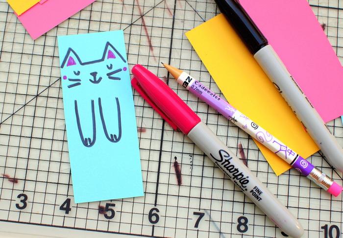 spalvotas popierius, katės veidas ir ant mėlyno popieriaus nupieštos letenos, ikimokyklinio amžiaus veikla, juodos ir rausvos spalvos aštrumai