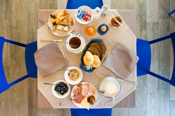 polna miza, s skodelicami kave in krožniki, skledo robidnic, zdravim tedenskim obrokom, modri stoli naokoli