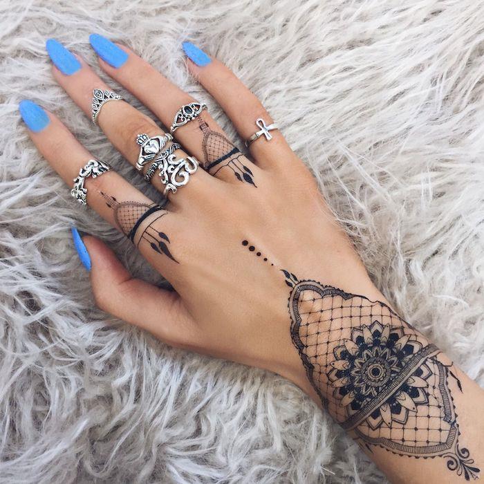 dolg modri lak za nohte, tetovaže mandale, ideje za tetoviranje prstov, veliko srebrnih prstanov, roka počiva na krzneni odeji