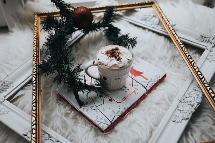 karštas šokoladas su gėrimu su daug šviežios grietinėlės, auksinis rėmelis, knyga, pušies šakelė ir raudonas Kalėdų kamuolys, Kalėdų fonas