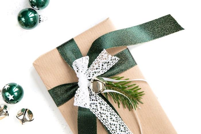 dovanų pakavimo dėžutė Kalėdoms iš kraftpopieriaus, pušies šakelės, žalios juostelės, baltos nėrinių juostelės ir varpų