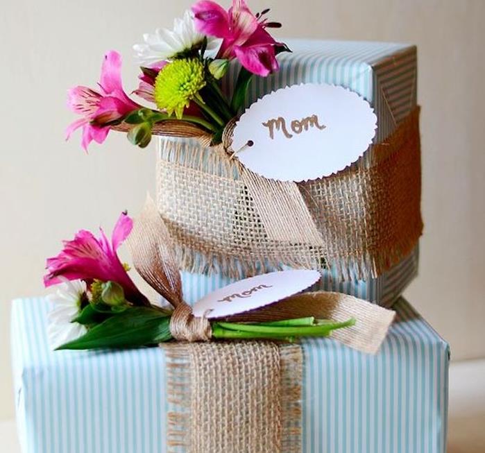 kartoninės dovanų dėžutės, įvyniotos į dovanų popierių su mėlynai baltomis juostelėmis ir gėlių puokšte, pavyzdys