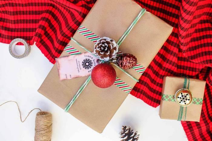 Kalėdų dovanų pakuotė, dėžutė, įvyniota į kraftpopierių su raudonų, baltų ir žalių skalbinių juostelių juostelėmis, pušies kūgis, ornamentas ir kalėdinė etiketė
