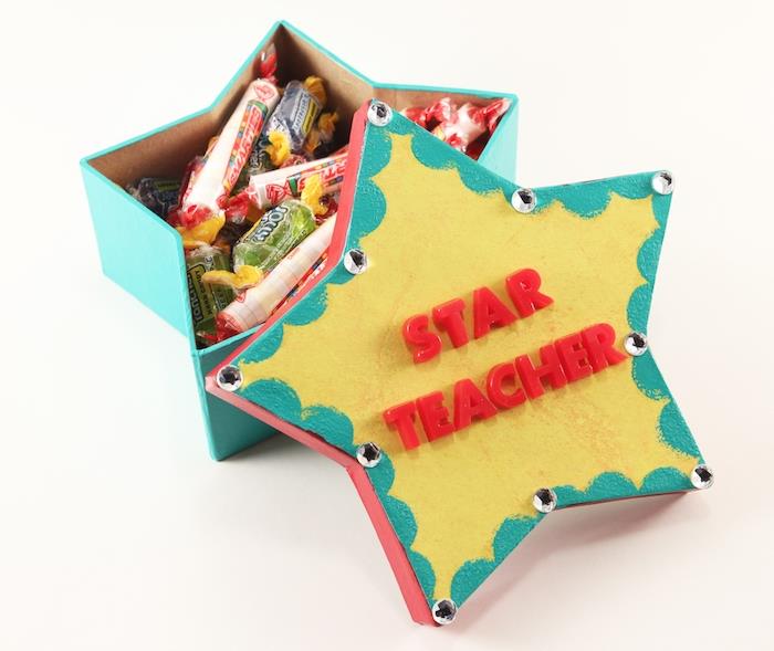 personalizuota dovanėlė centre, žvaigždės formos dėžutė, užpildyta saldainiais spalvingais vokais ir raudonomis raidėmis, ant kurių rašoma meilužė žvaigždė