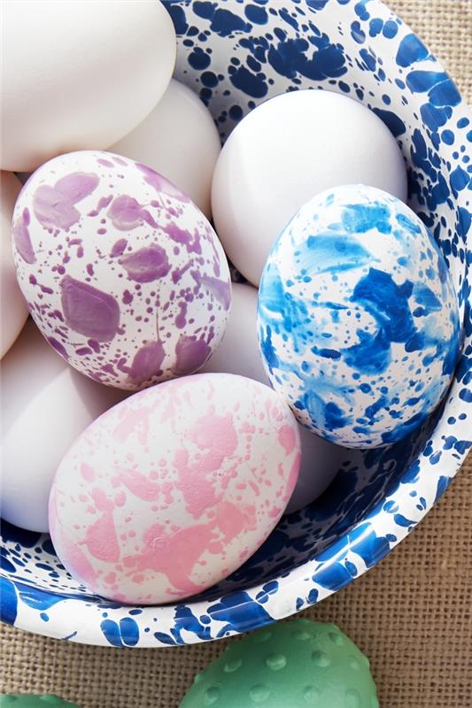 balto ir tamsiai mėlyno marmuro dizaino dubuo su balto lukšto kiaušiniais, dekoruotas spalvingais marmurinio dizaino valgomaisiais dažais