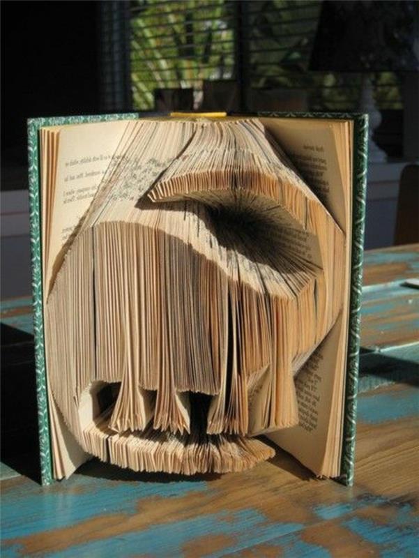 knjižna zložljivost, oblika dinozavra, narejena iz izrezanih in prepognjenih strani, v starodobni knjigi, z zeleno -belimi trdimi platnicami z vzorcem