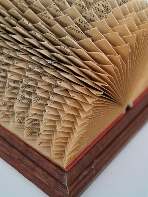 vzorci zlaganja knjig, starodobna knjiga z rdečimi platnicami, postavljena v leseni okvir, odprta, da razkrije zapleten geometrijski vzorec, narejen iz prepognjenih strani