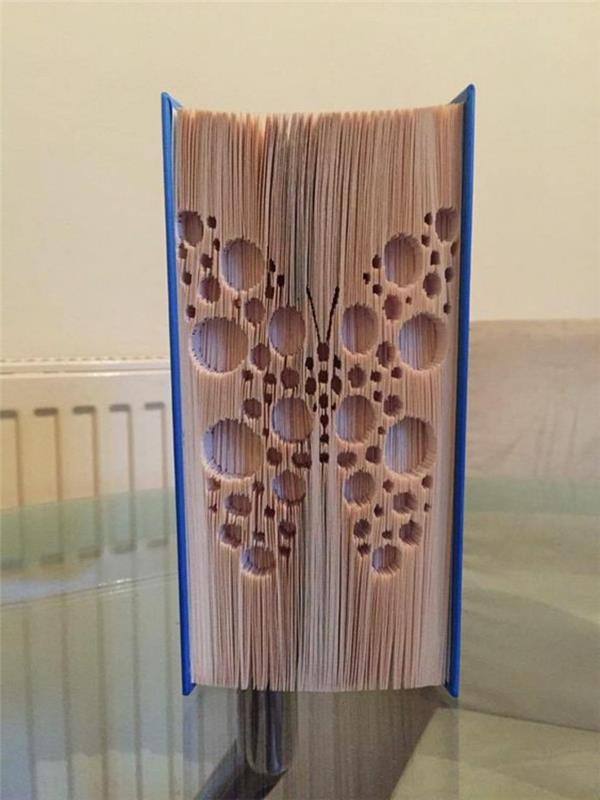 zaprta knjiga s trdimi modrimi platnicami, metulj iz geometrijskih oblik, vklesan na straneh