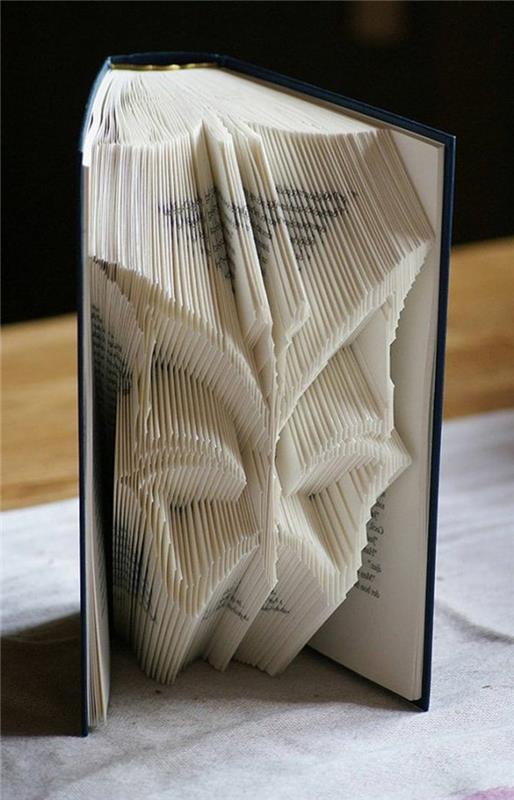 knjižni zgib, oblika metulja iz prepognjenih strani, v odprti knjigi s temno modrimi trdimi platnicami