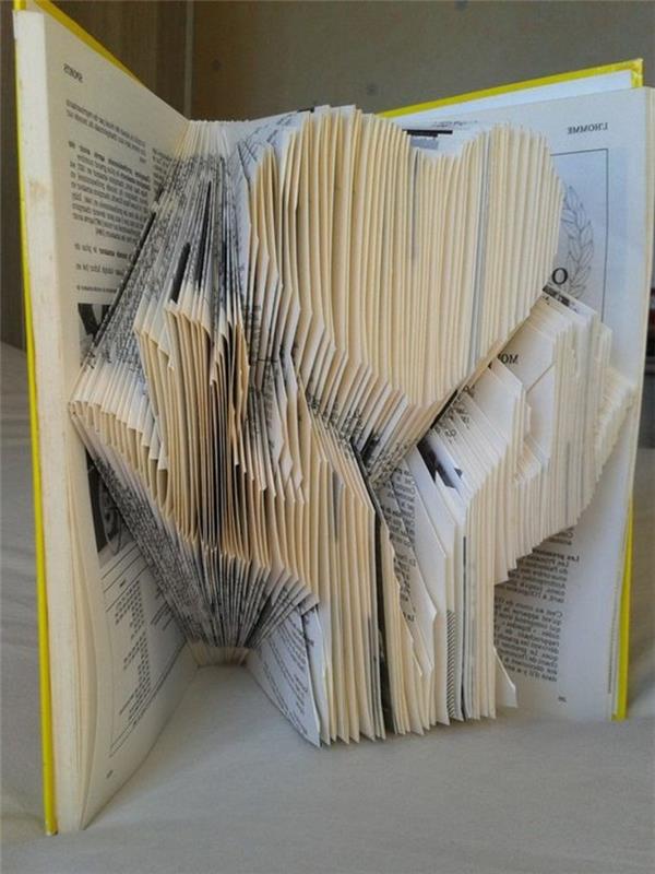knjižni zgib, 3D slika dveh rok z obliko srca v zloženih straneh, v odprti knjigi s trdimi rumenimi platnicami