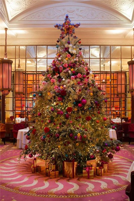 Božične kroglice in množica rož za okrasitev naravnega velikanskega božičnega drevesa z darilnimi paketi ob vznožju drevesa
