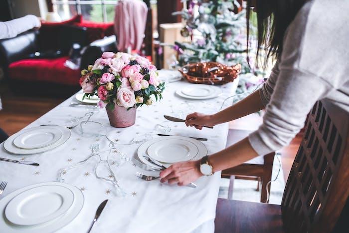 Zarif bir buket çiçek, beyaz masa örtüsü üzerinde hafif çelenk, beyaz tabaklar ile Noel merkezinde.