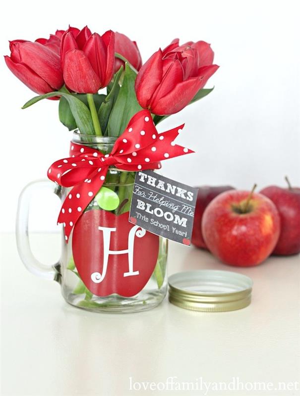 mokyklos dovana, idėja apie transformuotą stiklinę gėlių vazą su raudono obuolio raštu, žinių ir išminties simbolis bei tulpių puokštė