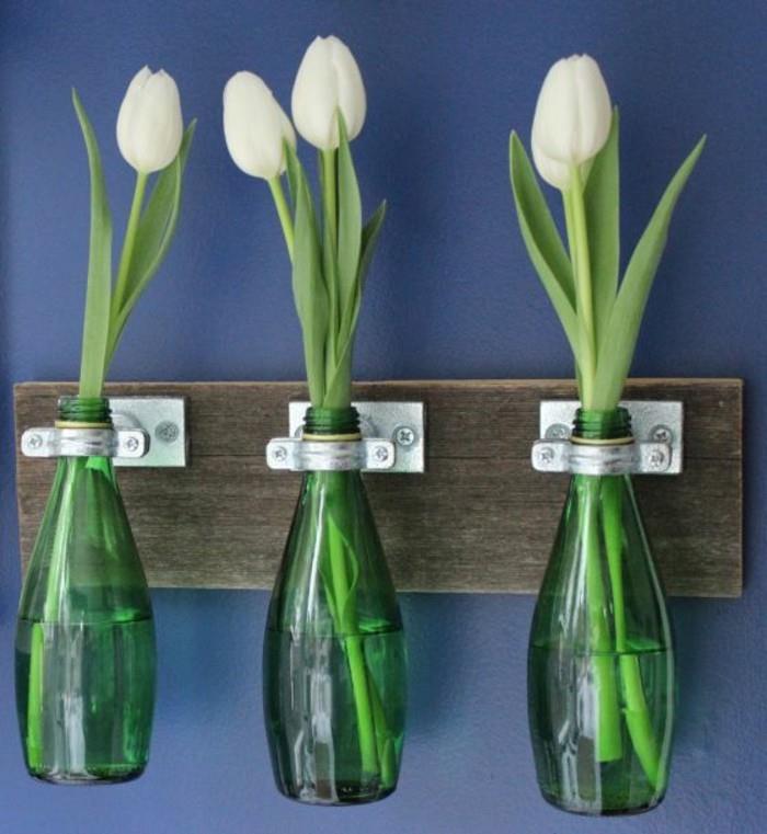 žalias butelis gėlių vazoje, pritvirtintas prie sienos