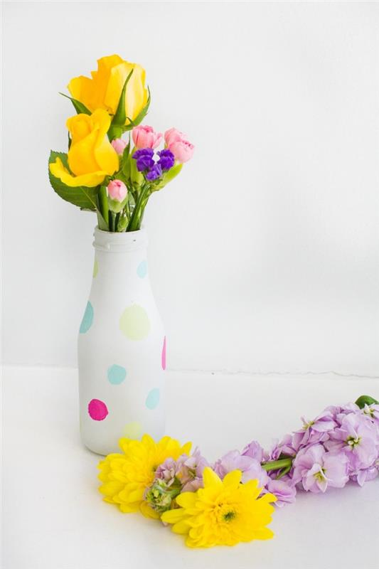 butelis paverstas vaza, dideli įvairiaspalviai taškeliai, geltonos rožės, gvazdikai, gimtadienio stalo puošmena