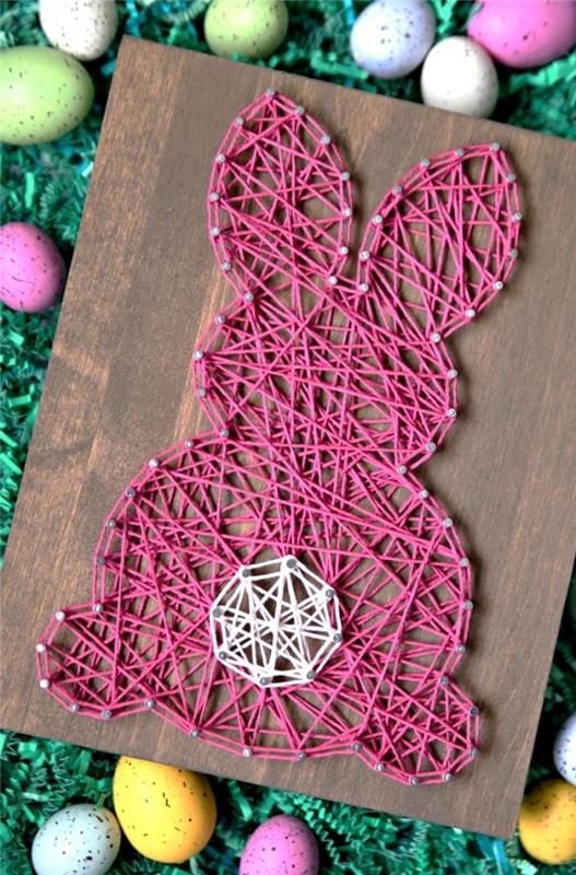 kokią Velykų dekoraciją gaminti su vaikais, tamsaus medžio stalo modelis, papuoštas rožiniais ir baltais siūlais triušio pavidalu