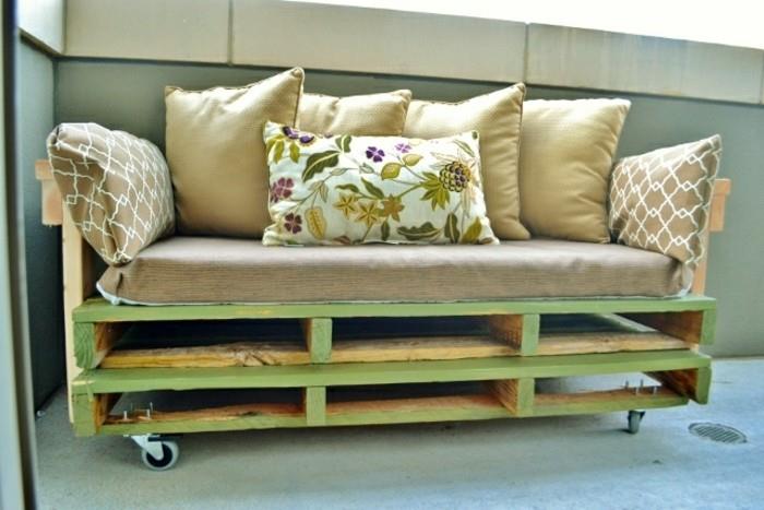 baldai, pagaminti iš padėklų, šviesiai žalia medinė sofa, padengta didele smėlio spalvos pagalve ir dekoruota keliomis mažesnėmis pagalvėlėmis