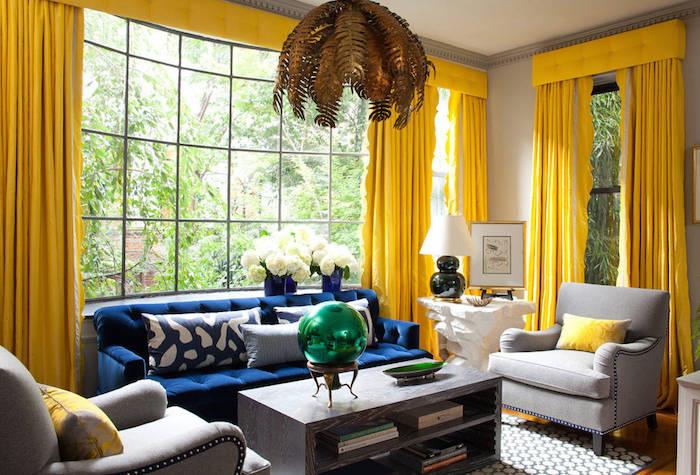ryškiai geltonos užuolaidos kambaryje su dideliais langais, svetainės spalvų idėjos, tamsiai mėlyna sofa ir šviesiai pilki foteliai, masyvus medinis kavos staliukas